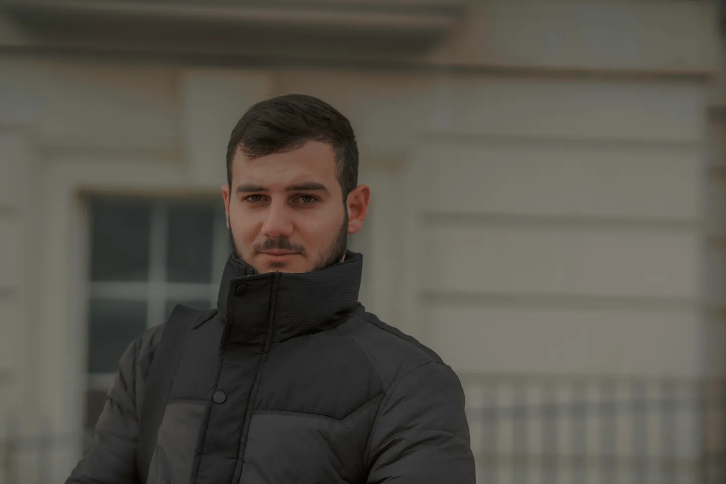 Provisional portrait of a man wearing a winter jacket against a blurred urban background.